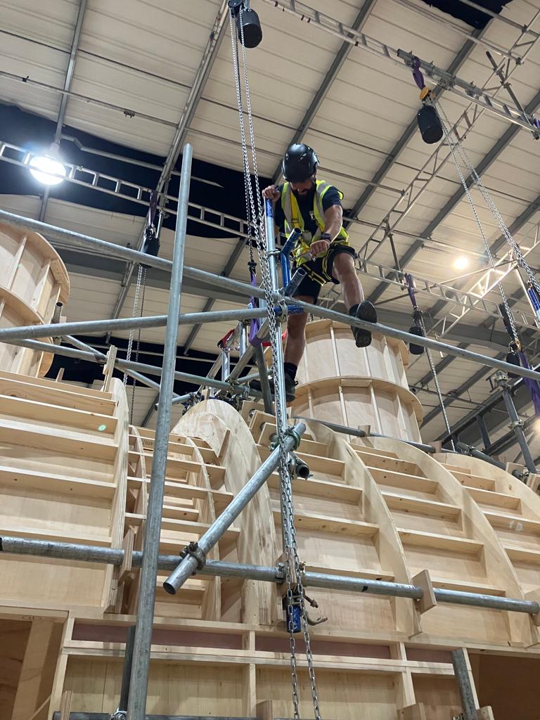A KBL rigger in harness and hi-vis working at height on scaffold during a studio set build