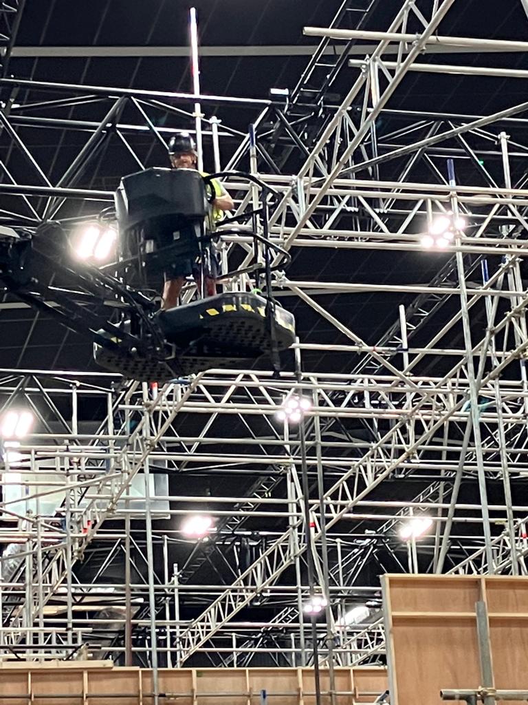 A rigger working from a cherry picker inside a dense overhead truss grid
